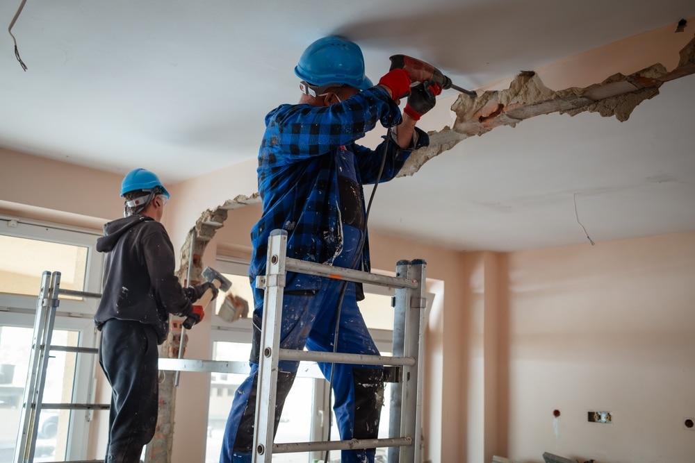Two Construction Workers On Scaffolding Demolishes A Wall
